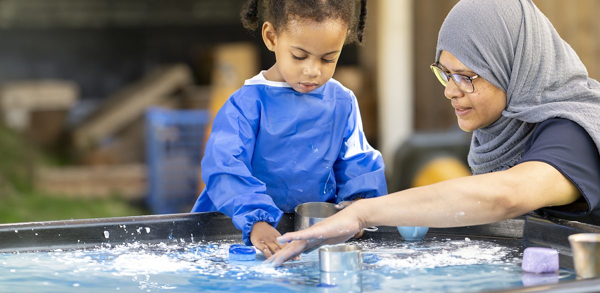 A nursery practitioner and a young child playing together at a water tray.