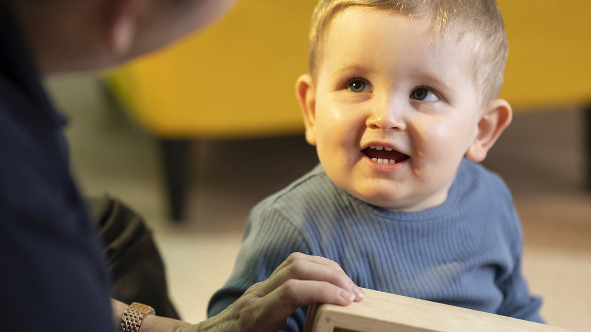 A smiling baby looking up at a nursery practitioner during play.