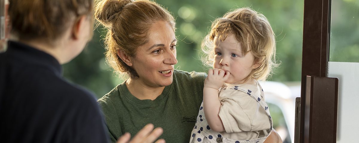 A parent holding their child while talking with a nursery practitioner at the door.