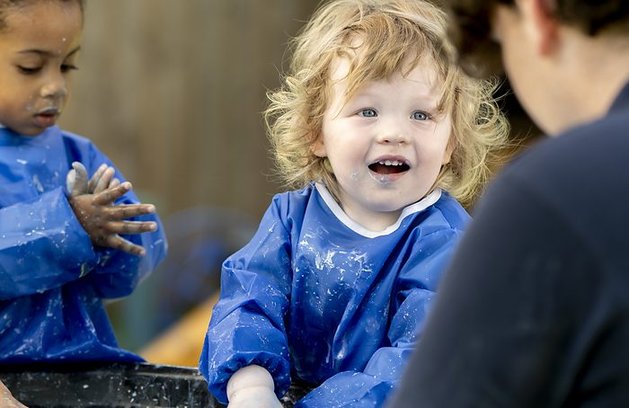 A smiling toddler in a painting apron during a messy play activity.